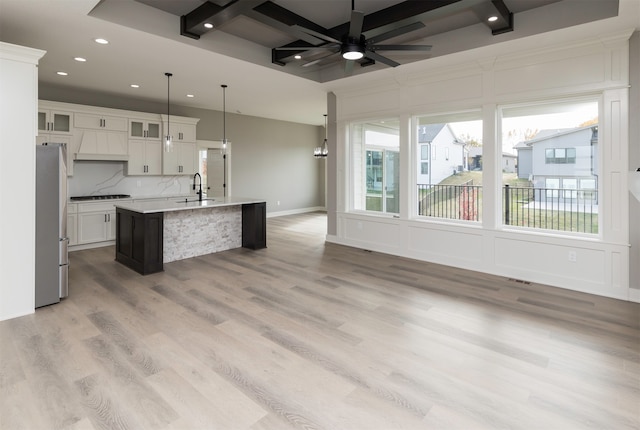 kitchen featuring a kitchen island with sink, wood-type flooring, sink, pendant lighting, and white cabinets