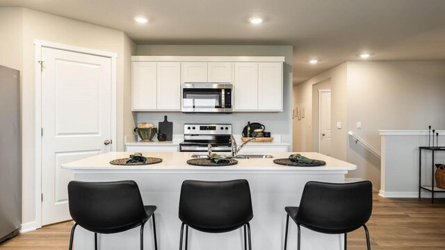 kitchen featuring light wood-type flooring, stainless steel appliances, white cabinetry, and an island with sink