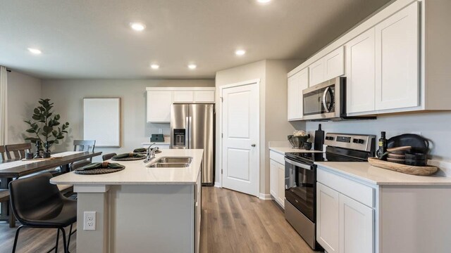 kitchen featuring white cabinets, a center island with sink, light wood-type flooring, and appliances with stainless steel finishes