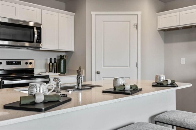 kitchen featuring white cabinets, appliances with stainless steel finishes, light stone counters, and sink