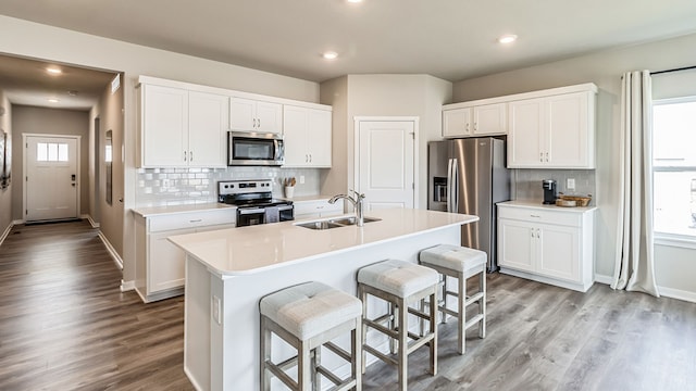 kitchen with sink, appliances with stainless steel finishes, an island with sink, white cabinets, and light wood-type flooring