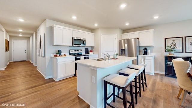 kitchen with a center island with sink, white cabinets, appliances with stainless steel finishes, light hardwood / wood-style floors, and a breakfast bar area