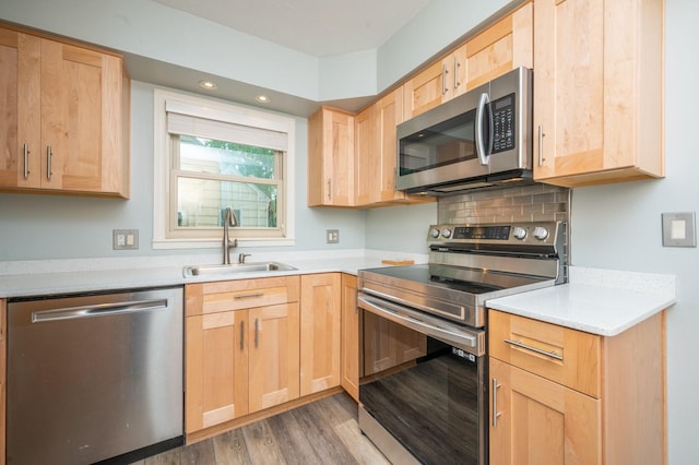 kitchen featuring light wood finished floors, tasteful backsplash, light brown cabinets, appliances with stainless steel finishes, and a sink