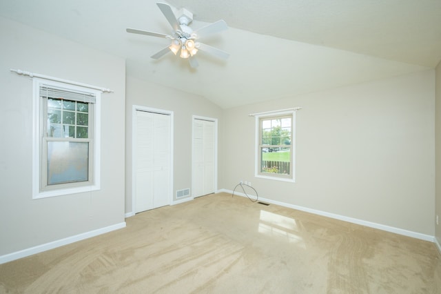 unfurnished bedroom featuring ceiling fan, light colored carpet, two closets, and vaulted ceiling