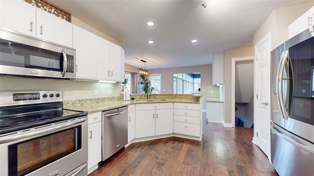 kitchen featuring white cabinets, kitchen peninsula, hanging light fixtures, appliances with stainless steel finishes, and dark hardwood / wood-style flooring