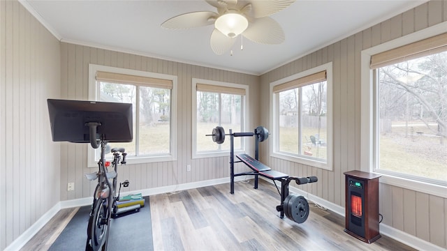 exercise room with wooden walls, ornamental molding, ceiling fan, and light hardwood / wood-style flooring