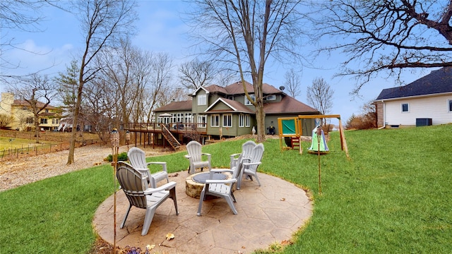 rear view of house featuring a playground, a fire pit, a wooden deck, a lawn, and a patio area