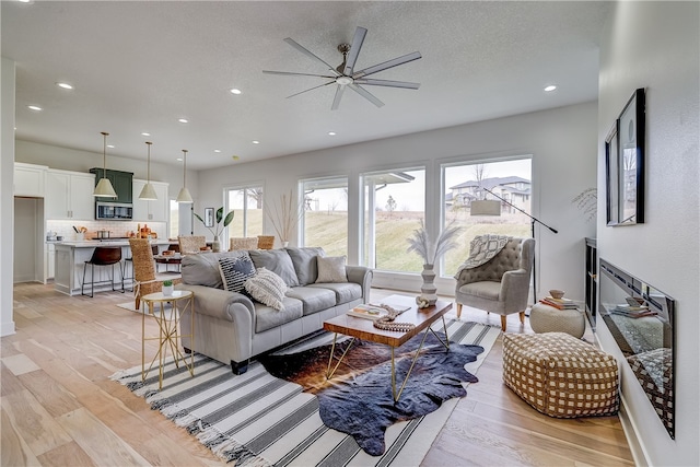 living room with a textured ceiling, light hardwood / wood-style floors, and ceiling fan