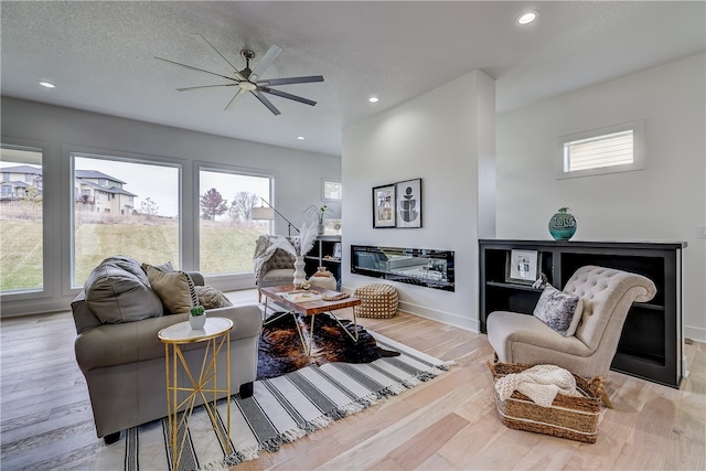 living room with ceiling fan, a textured ceiling, light hardwood / wood-style flooring, and plenty of natural light