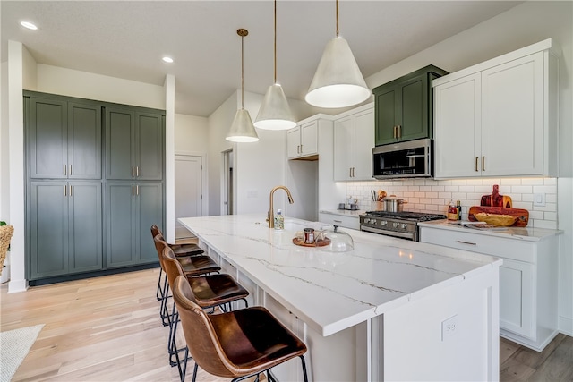 kitchen with pendant lighting, stainless steel appliances, light hardwood / wood-style floors, and a center island with sink