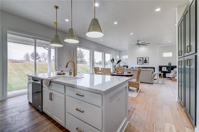 kitchen featuring a healthy amount of sunlight, a kitchen island with sink, light stone countertops, and pendant lighting