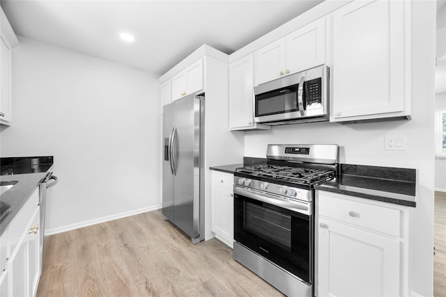 kitchen with white cabinetry, appliances with stainless steel finishes, light hardwood / wood-style flooring, and dark stone counters