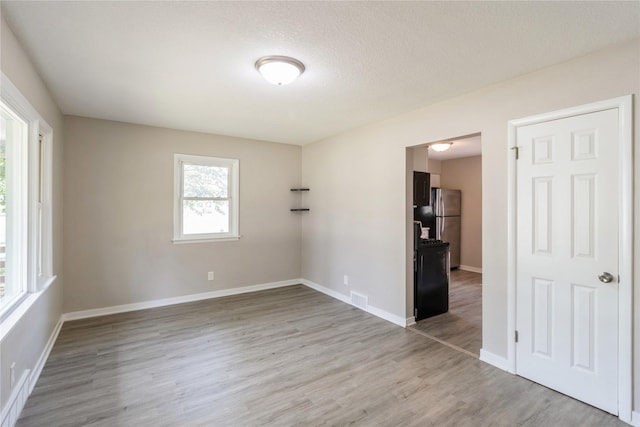 unfurnished room with baseboards, a textured ceiling, visible vents, and wood finished floors