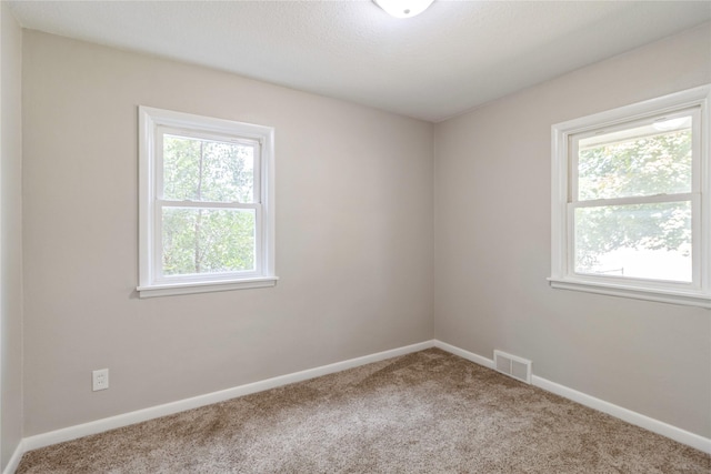 carpeted empty room featuring baseboards and visible vents