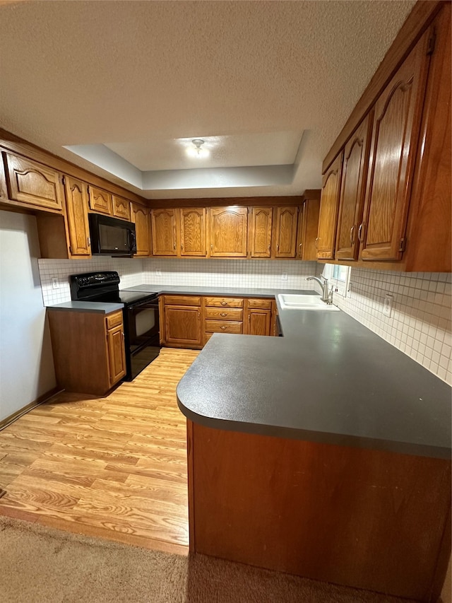 kitchen featuring decorative backsplash, light hardwood / wood-style floors, black appliances, a tray ceiling, and sink