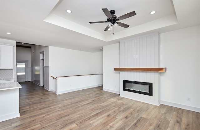 unfurnished living room with a fireplace, ceiling fan, a raised ceiling, and light hardwood / wood-style flooring