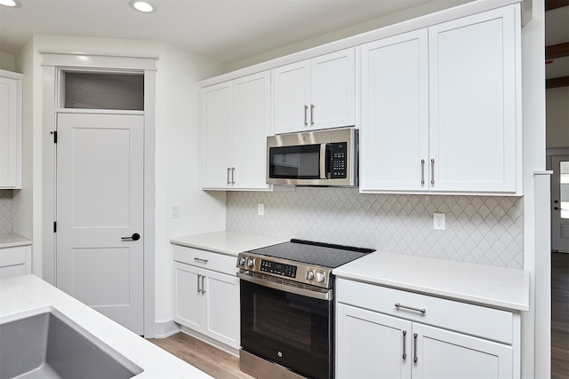 kitchen featuring backsplash, appliances with stainless steel finishes, light wood-type flooring, and white cabinetry