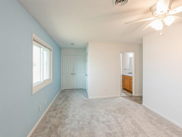 unfurnished bedroom featuring ensuite bathroom, ceiling fan, light carpet, a textured ceiling, and a closet