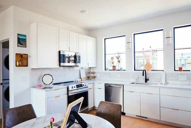 kitchen with appliances with stainless steel finishes, light hardwood / wood-style floors, white cabinets, stacked washer and dryer, and sink