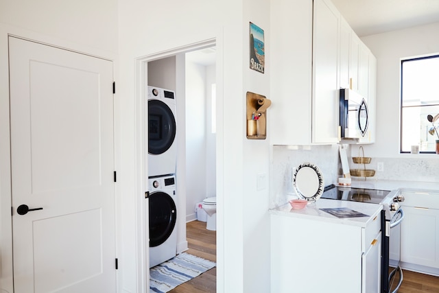 interior space featuring appliances with stainless steel finishes, stacked washer and clothes dryer, dark hardwood / wood-style floors, and white cabinets