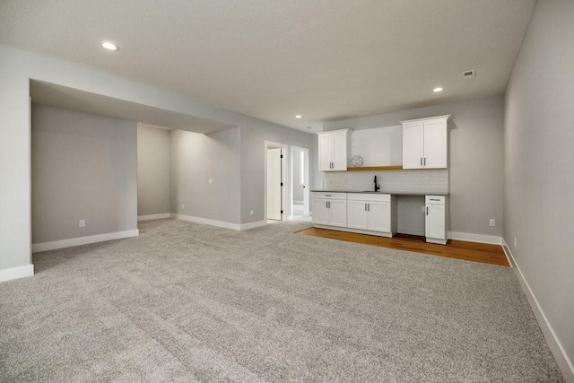 unfurnished living room with light carpet, sink, and built in desk