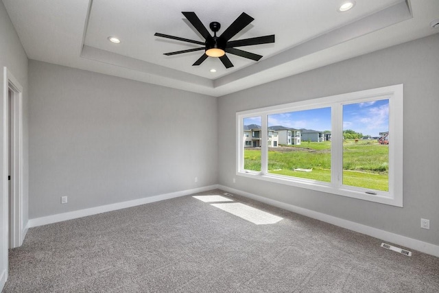 unfurnished room featuring a raised ceiling, carpet floors, and ceiling fan