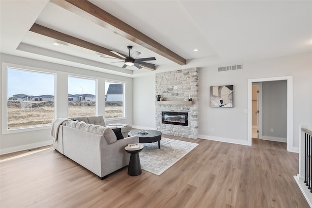 living room featuring ceiling fan, a fireplace, light hardwood / wood-style floors, and beam ceiling