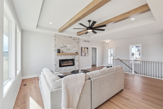 living room featuring a fireplace, ceiling fan, a raised ceiling, beam ceiling, and light hardwood / wood-style flooring