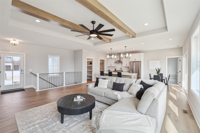 living room featuring an inviting chandelier, a tray ceiling, light hardwood / wood-style flooring, and beam ceiling