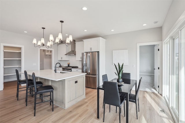 kitchen featuring appliances with stainless steel finishes, pendant lighting, white cabinetry, a center island with sink, and wall chimney exhaust hood