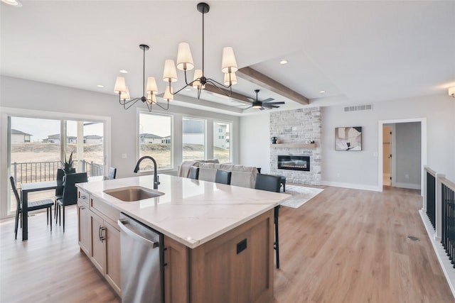 kitchen with sink, a stone fireplace, light stone countertops, decorative light fixtures, and stainless steel dishwasher