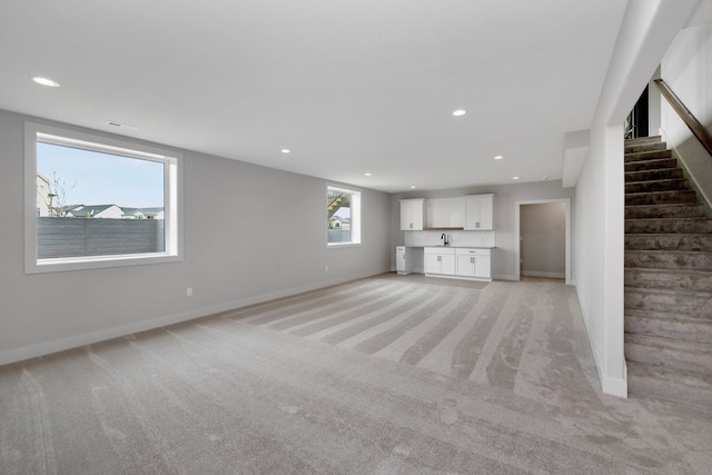 unfurnished living room featuring a healthy amount of sunlight, light colored carpet, and sink