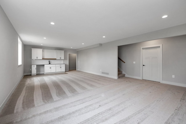 unfurnished living room featuring built in desk, sink, and light carpet