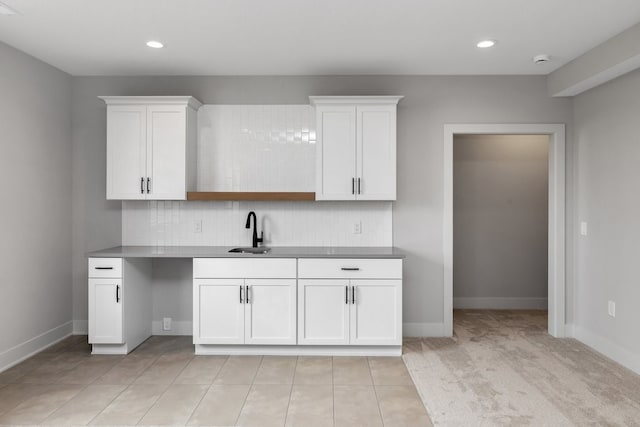 kitchen featuring light carpet, decorative backsplash, white cabinetry, and sink