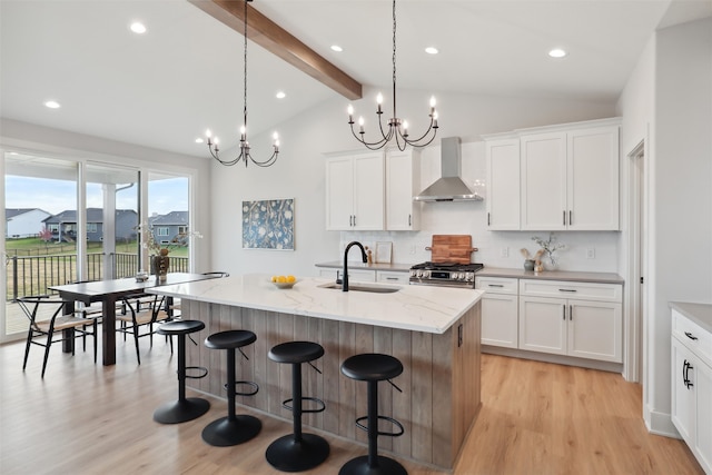 kitchen with wall chimney exhaust hood, sink, vaulted ceiling with beams, and an island with sink