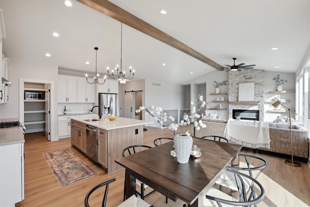 dining room featuring sink, light wood-type flooring, a barn door, lofted ceiling with beams, and a stone fireplace