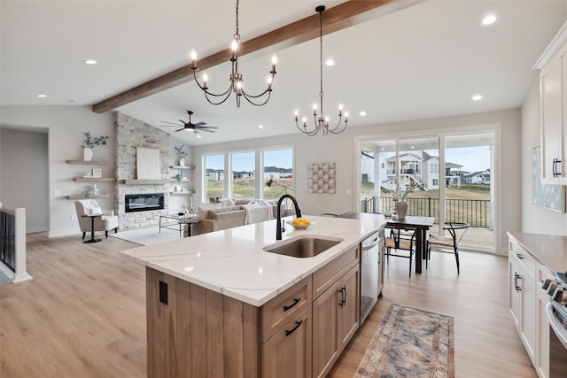 kitchen with sink, lofted ceiling with beams, a stone fireplace, hanging light fixtures, and a kitchen island with sink