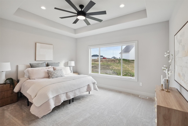 carpeted bedroom with a tray ceiling and ceiling fan