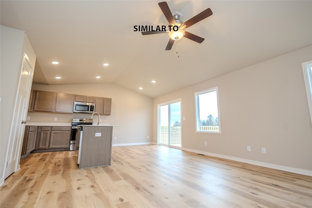 kitchen featuring an island with sink, light hardwood / wood-style floors, stainless steel appliances, ceiling fan, and vaulted ceiling