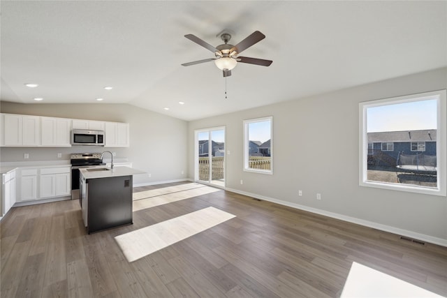 kitchen with lofted ceiling, wood-type flooring, white cabinetry, stainless steel appliances, and a kitchen island with sink