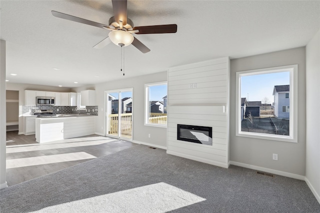 unfurnished living room with ceiling fan, light colored carpet, plenty of natural light, and a fireplace