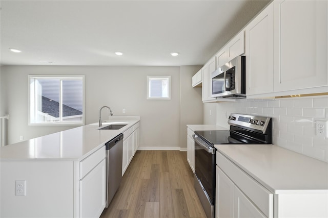 kitchen with appliances with stainless steel finishes, a peninsula, a sink, light countertops, and backsplash