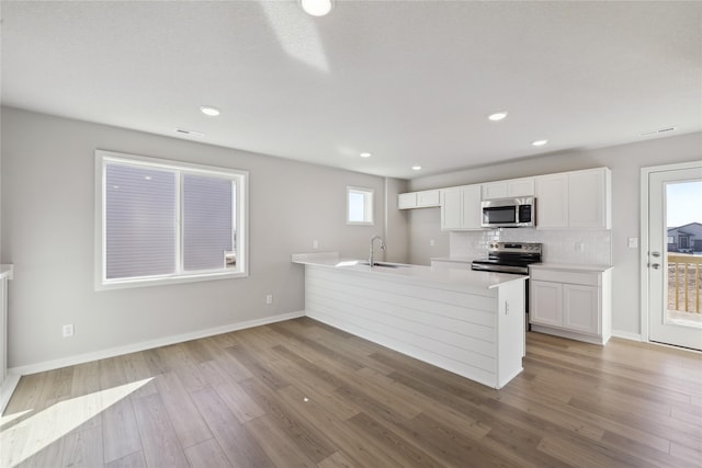 kitchen with light wood finished floors, appliances with stainless steel finishes, a peninsula, white cabinetry, and a sink