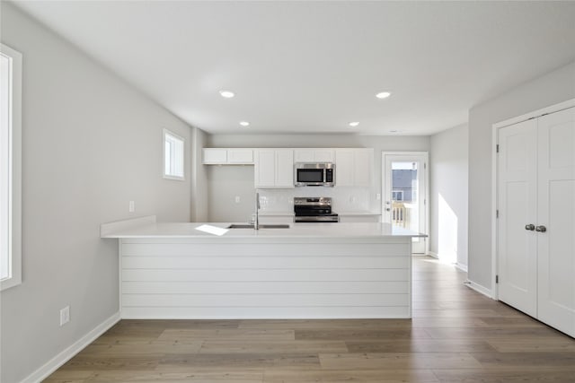 kitchen featuring stainless steel appliances, white cabinetry, a sink, wood finished floors, and a peninsula