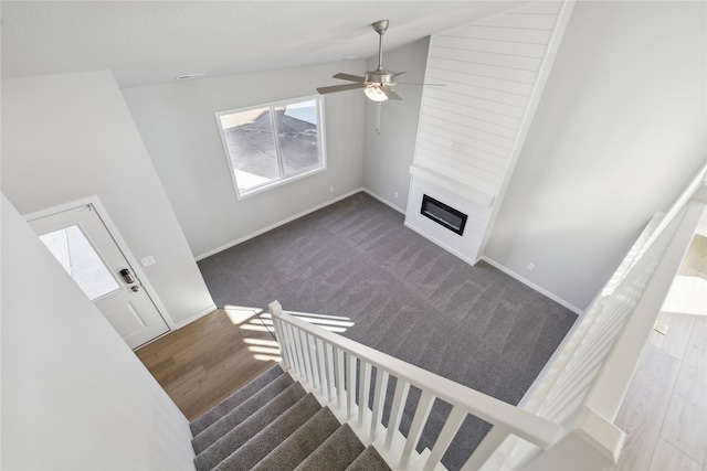 staircase featuring lofted ceiling, a large fireplace, ceiling fan, wood finished floors, and baseboards