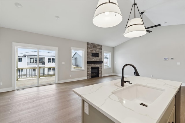 kitchen featuring light stone counters, vaulted ceiling, sink, decorative light fixtures, and an island with sink