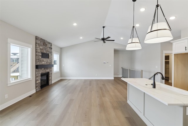 kitchen featuring vaulted ceiling, light stone countertops, a fireplace, decorative light fixtures, and white cabinetry