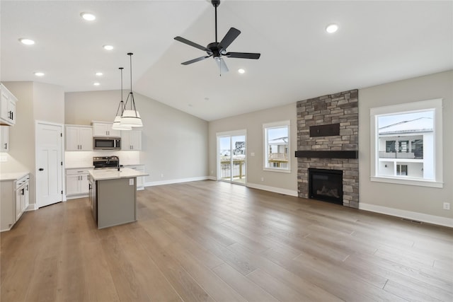 kitchen with pendant lighting, lofted ceiling, a kitchen island with sink, appliances with stainless steel finishes, and white cabinetry