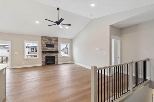 unfurnished living room with wood-type flooring, a stone fireplace, ceiling fan, and lofted ceiling