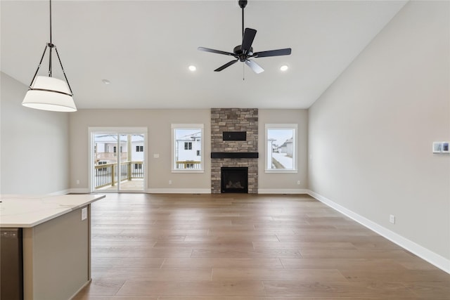 unfurnished living room featuring hardwood / wood-style flooring, a stone fireplace, and ceiling fan